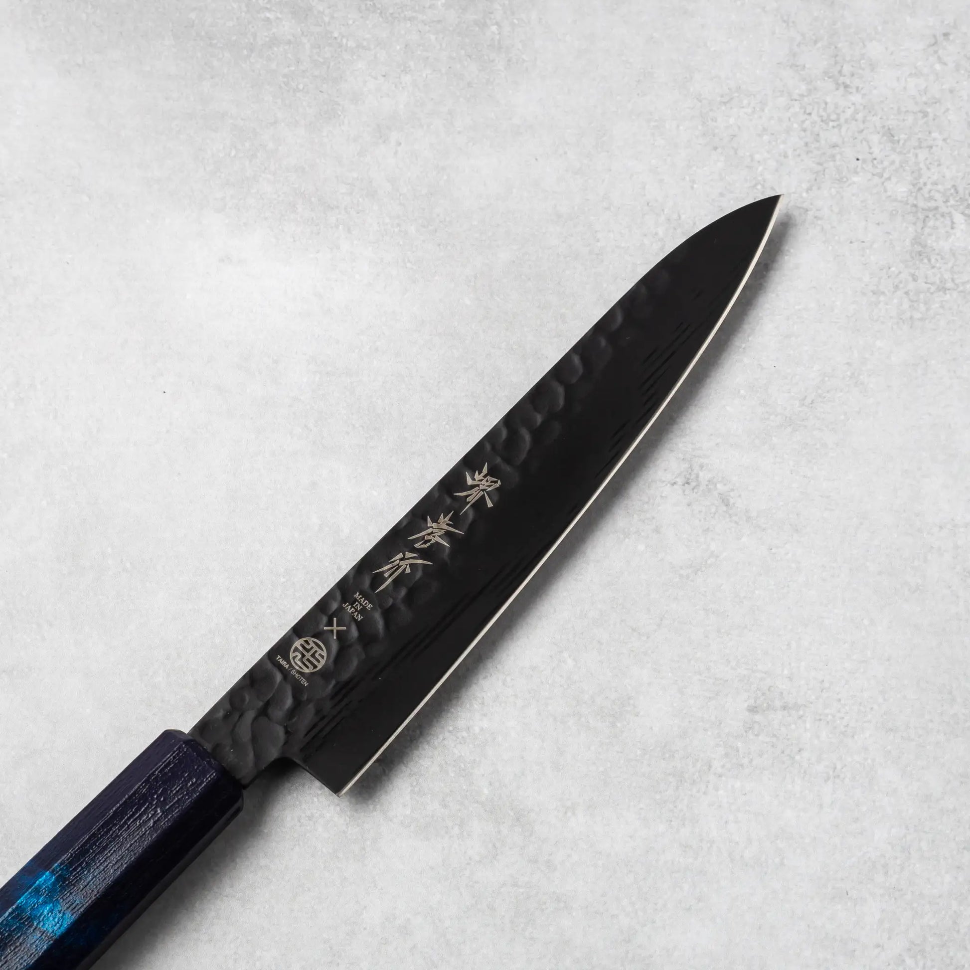 Close-up view of the Sakai Takayuki Kurokage VG10 petty knife's blade, highlighting the hammered texture and engraved Japanese kanji lettering.