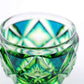 Close-up of intricate cyan yellow green Satsuma Kiriko two-tone sake cup, featuring geometric and starburst designs.