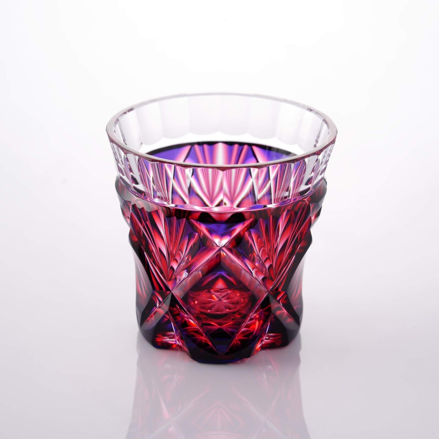 Satsuma Kiriko two-tone sake cup with geometric red and purple patterns against a reflective surface.