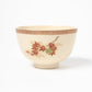 Side view of a cream-colored matcha bowl adorned with vibrant red and green maple leaves, accented by a decorative border near the rim.