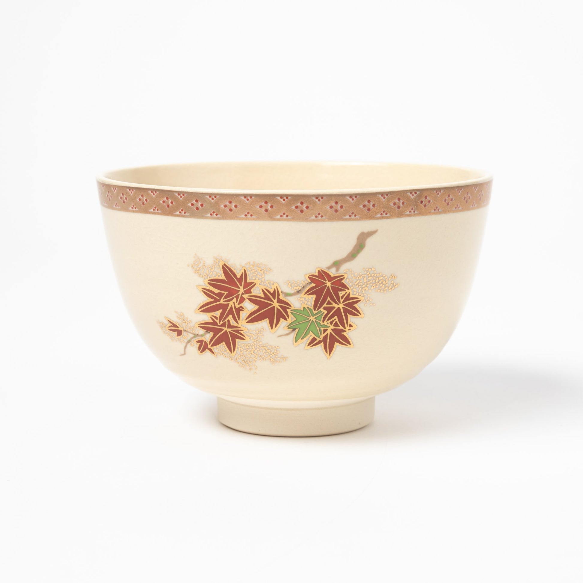 Side view of a cream-colored matcha bowl adorned with vibrant red and green maple leaves, accented by a decorative border near the rim.