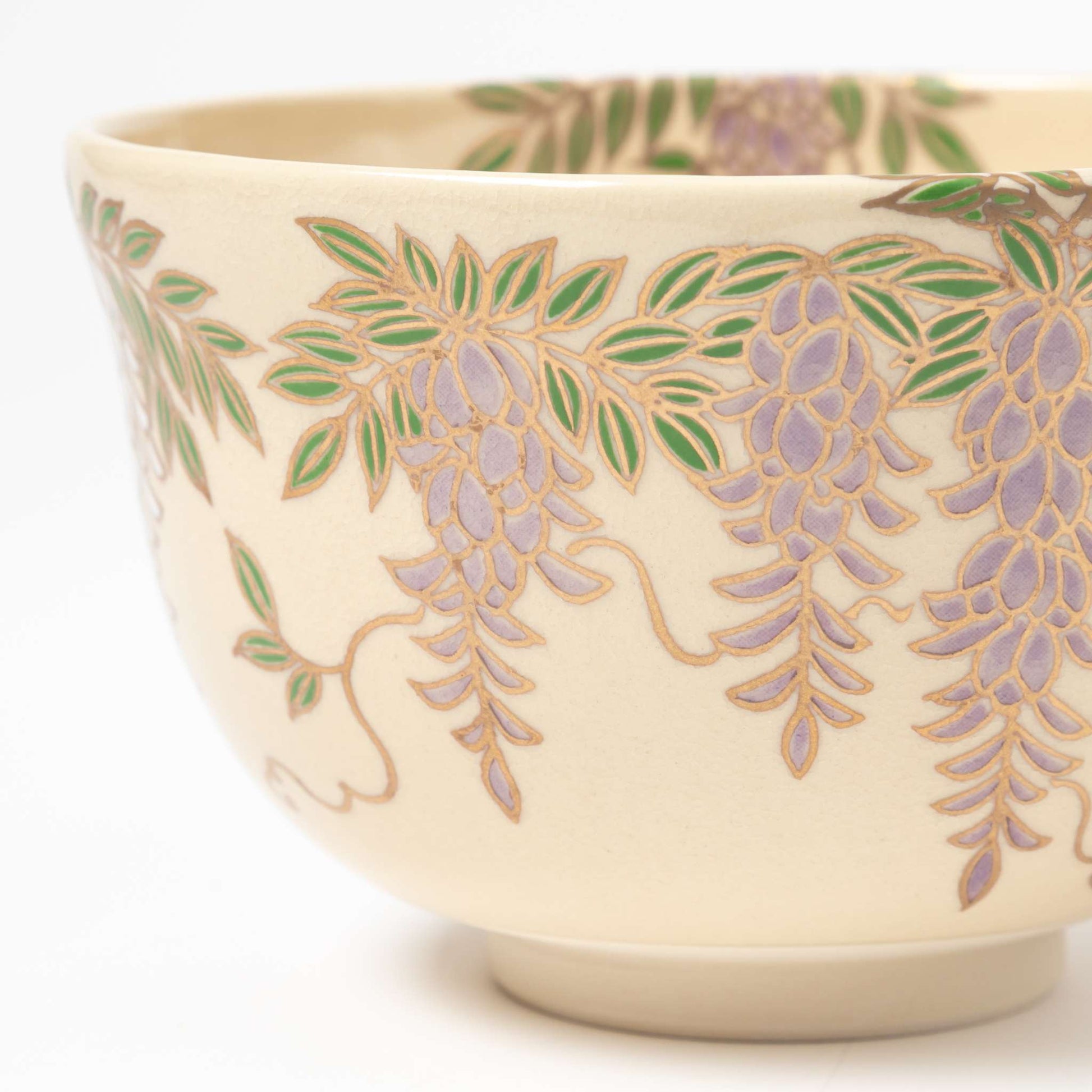 Detailed side view of a matcha bowl highlighting the beautifully hand-painted wisteria vines and leaves in green and purple.