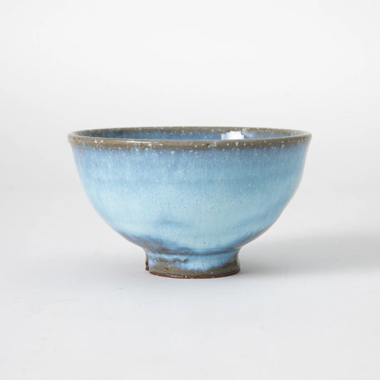 A Hagi ware matcha bowl by Senryuzan with a soft sky blue glaze, fine white speckles across the surface, a warm grey clay rim, and a small raised foot, photographed from the side against a white background.