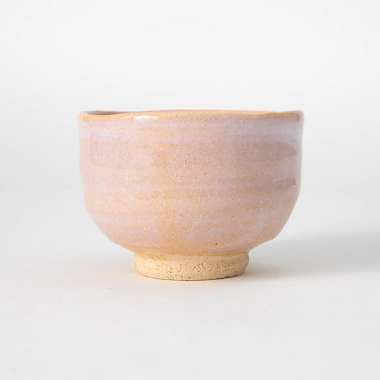A Hagi ware matcha bowl by Senryuzan in daido sand clay with a soft blush biwa glaze fading toward the lower body, an unglazed sandy foot ring, and a wide gently curved form, photographed against a white background.