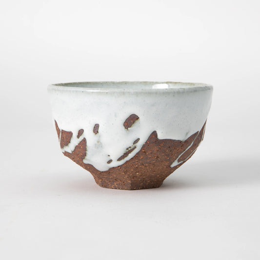 A Hagi ware matcha bowl by Senryuzan with a pale celadon white glaze on the upper body and interior, an irregular glaze boundary with drips and pools, and a deeply iron red carved unglazed lower body and foot, photographed against a white background.