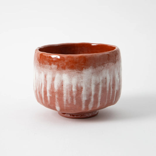 A hand built red raku matcha bowl by Shoraku Kiln in the Chojiro Jirobo style, with a rounded waist, inward turning rim, subtle asymmetry, deep terracotta red glaze, and white glaze in vertical passages across the exterior, photographed against a white background.