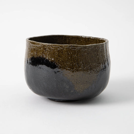 A hand built black raku matcha bowl by Shoraku Kiln in the Koetsu Shigure style, with a half cylinder form, gently rounded waist, flat finished rim, and black glaze thinning to reveal dark brownish clay beneath across the surface, photographed against a white background.