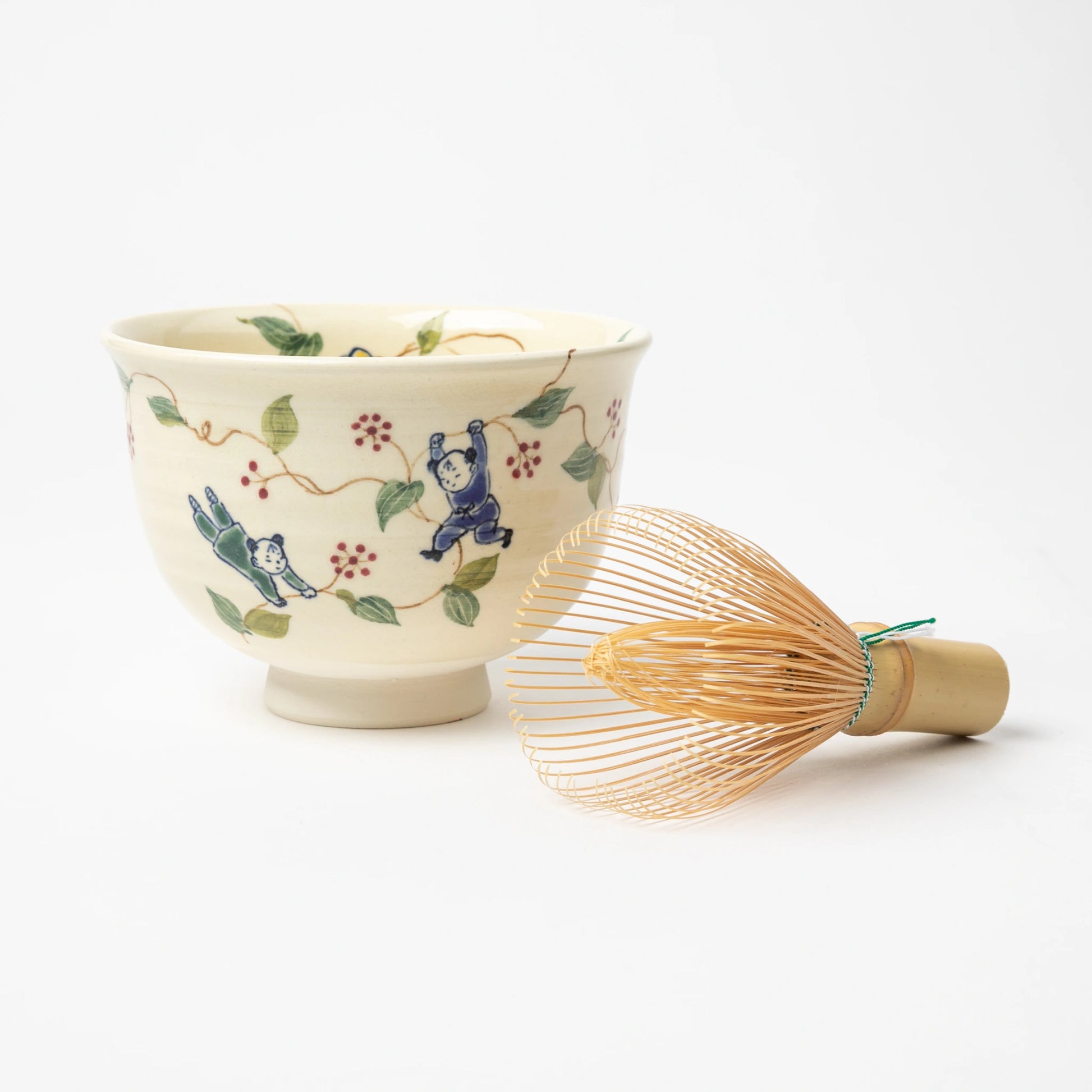 A handcrafted Karako and Sankirai Matcha Bowl by Tosen Kiln, featuring playful Karako children among green vines and red berries on an ivory background, displaying with matcha whisk.