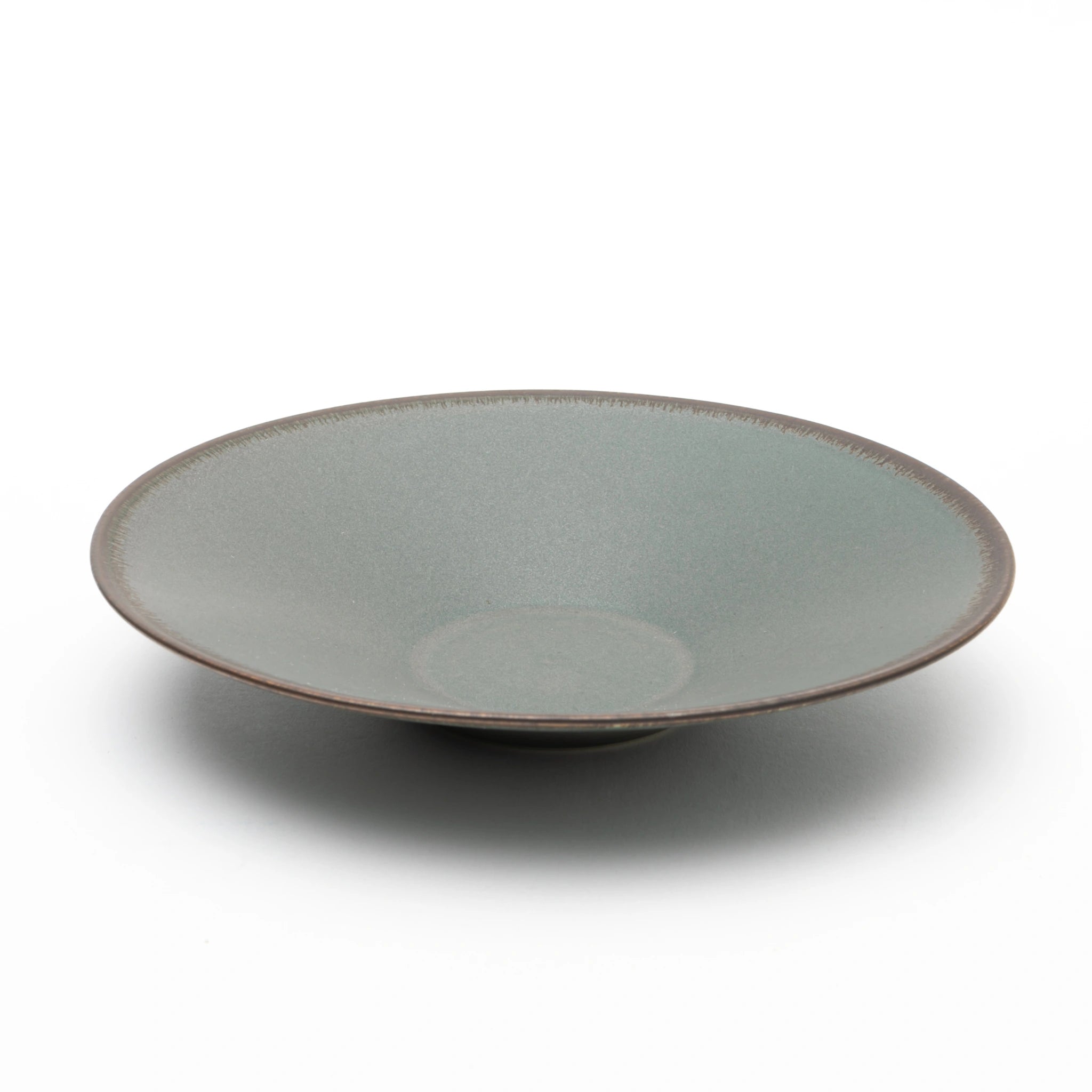 Three-quarter view of the Tsukamoto Mashiko ware SABI flat bowl in deep green, showing a wide shallow form with a matte, vintage-finish glaze across the interior and dark clay body visible at the rim edge.