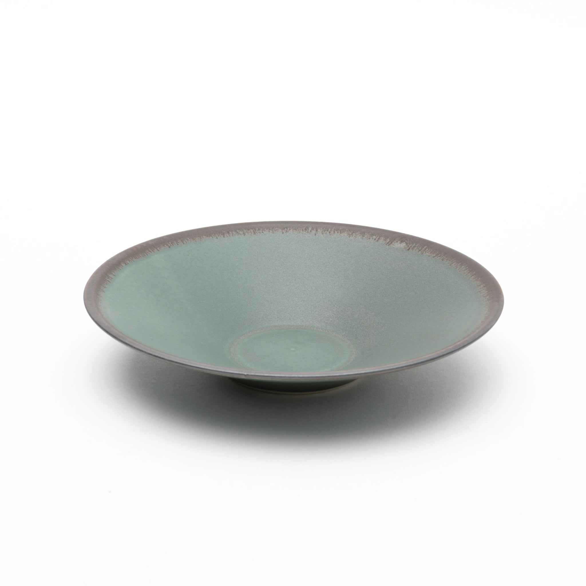 Three-quarter view of the Tsukamoto Mashiko ware SABI flat bowl medium in deep green, showing a wide shallow form with a matte, vintage-finish glaze across the interior and dark clay body visible at the rim edge.