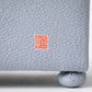 Detailed view of the Kaga Yuzen Michinaga Accessory Box exterior fabric texture, displaying a red Hisatsune seal mark on a light grey background.