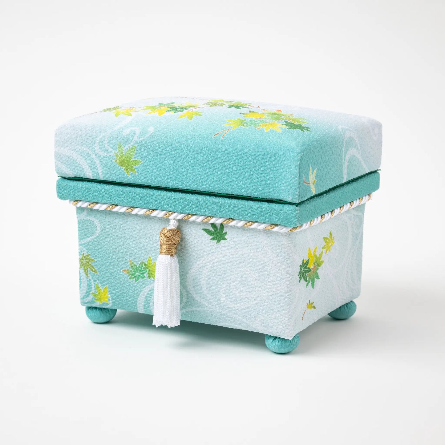 Kaga Yuzen Maple Leaf Accessory Box with lid on, highlighting the vibrant maple leaf design and decorative tassel, set on a mint green fabric with subtle wave patterns.