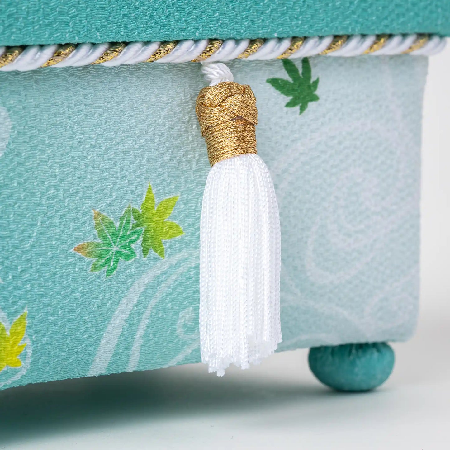 Detailed shot of the decorative white tassel and green fabric on the Kaga Yuzen Maple Leaf Accessory Box, with maple leaf motifs in shades of green and yellow.