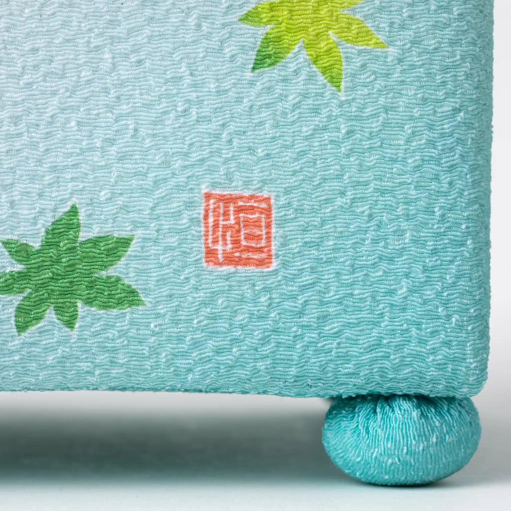 Close-up of the side of the Kaga Yuzen Maple Leaf Accessory Box, showing a delicate red seal on the mint green fabric adorned with maple leaves.