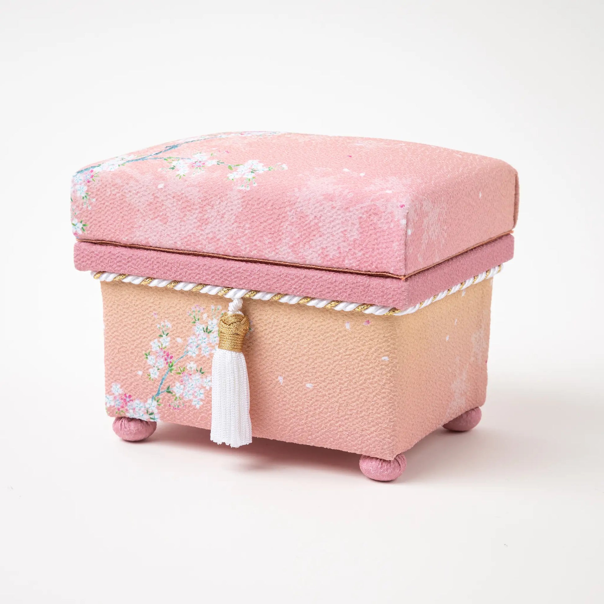 Angled view of the hisatsune YUZEN Kaga Yuzen Sakura accessory box, emphasizing the sakura design, white tassel, and the textured pink fabric.