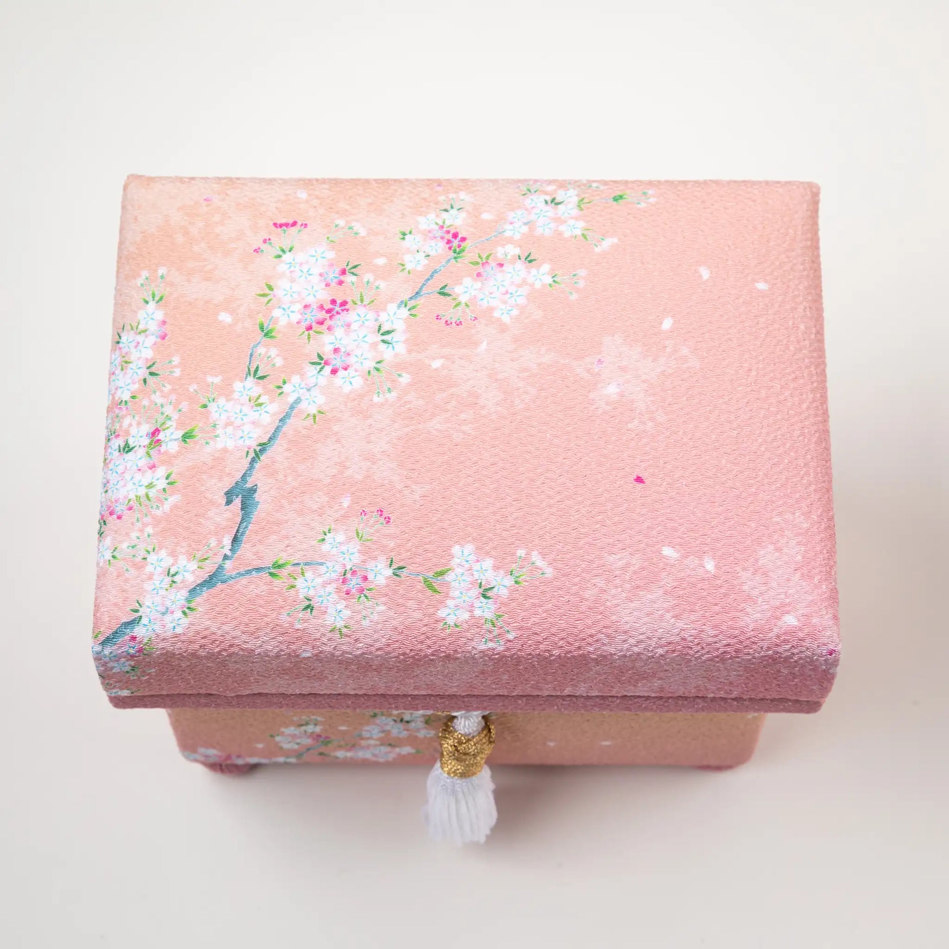 Top view of hisatsune YUZEN Kaga Yuzen Sakura accessory box in soft pink, adorned with delicate sakura (cherry blossom) patterns and a decorative white tassel.