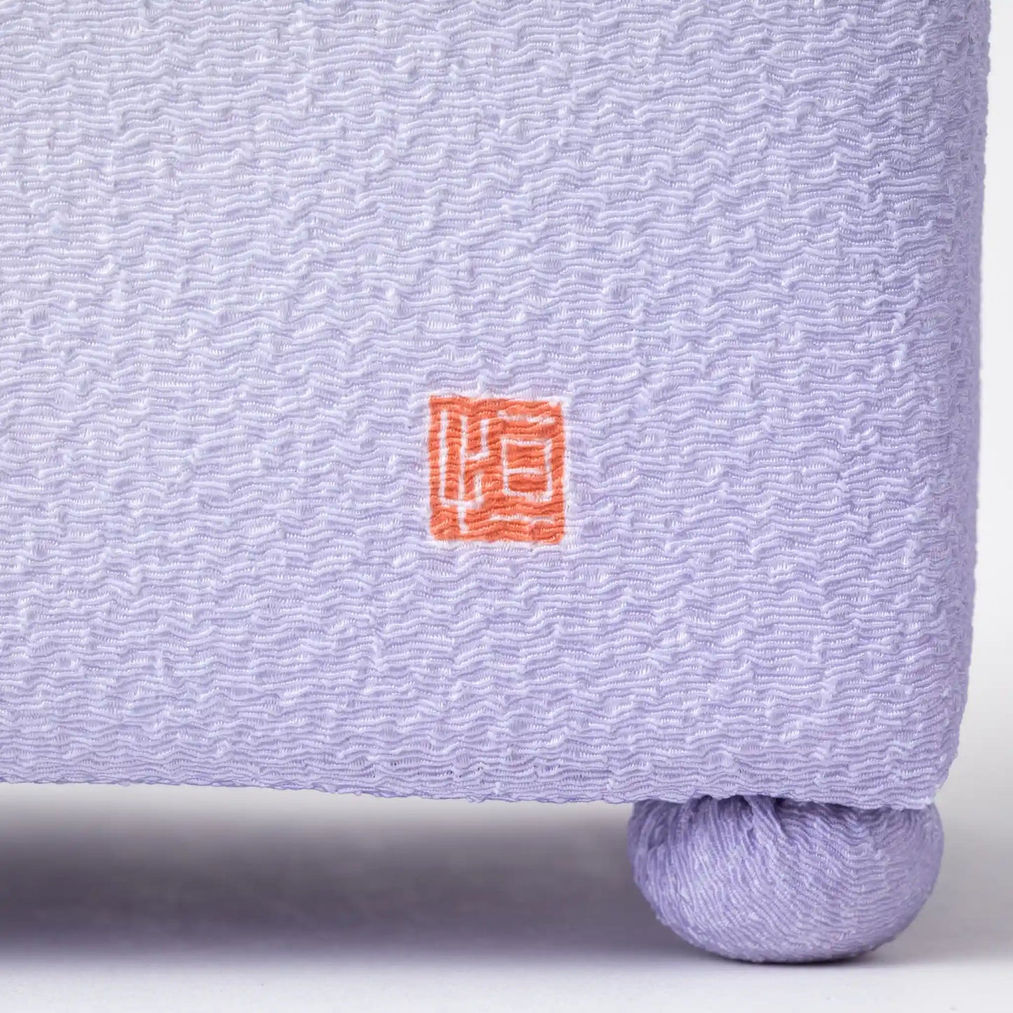 Close-up of the lower side of the Kaga Yuzen Wisteria Accessory Box, showing the delicate wavy texture with the brand's red stamp and a soft lavender hue on a rounded footed base.